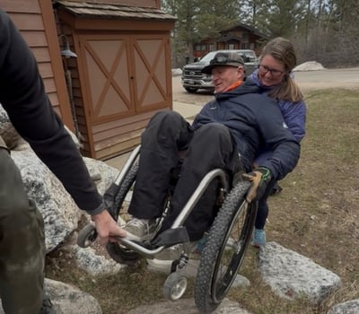 Heather assisting in maneuvering Geoff's wheelchair over rocky terrain.