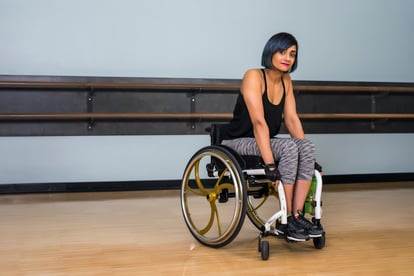 Woman in wheelchair wearing workout clothing in gym.