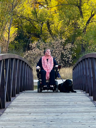 Elizabeth and her dog on a walking bridge. Elizabeth is using a wheelchair.