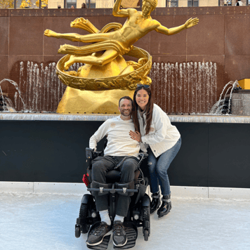 Hanna and Jerod ice skating at Rockefeller Center. Jerod is using a wheelchair and Hanna standing next to him.
