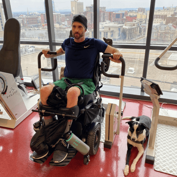 Jerod working out with his dog by his side. Jerod is using a wheelchair and wearing a beanie.
