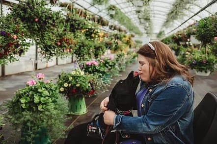 Katie and her service dog Petunia kiss in a greenhouse.