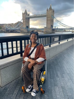 Curran sits in her wheelchair, smiling, in front of the Tower Bridge in London.