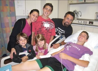 Zack laying in a hospital bed with his family around him