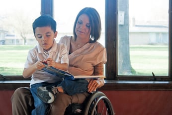woman in a wheelchair with her young son on her lap reading