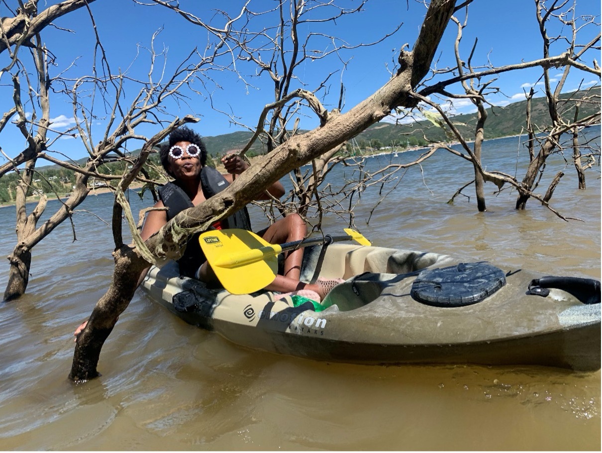 Curran, in a kayak on the water, wearing sunglasses and making a kissy face.