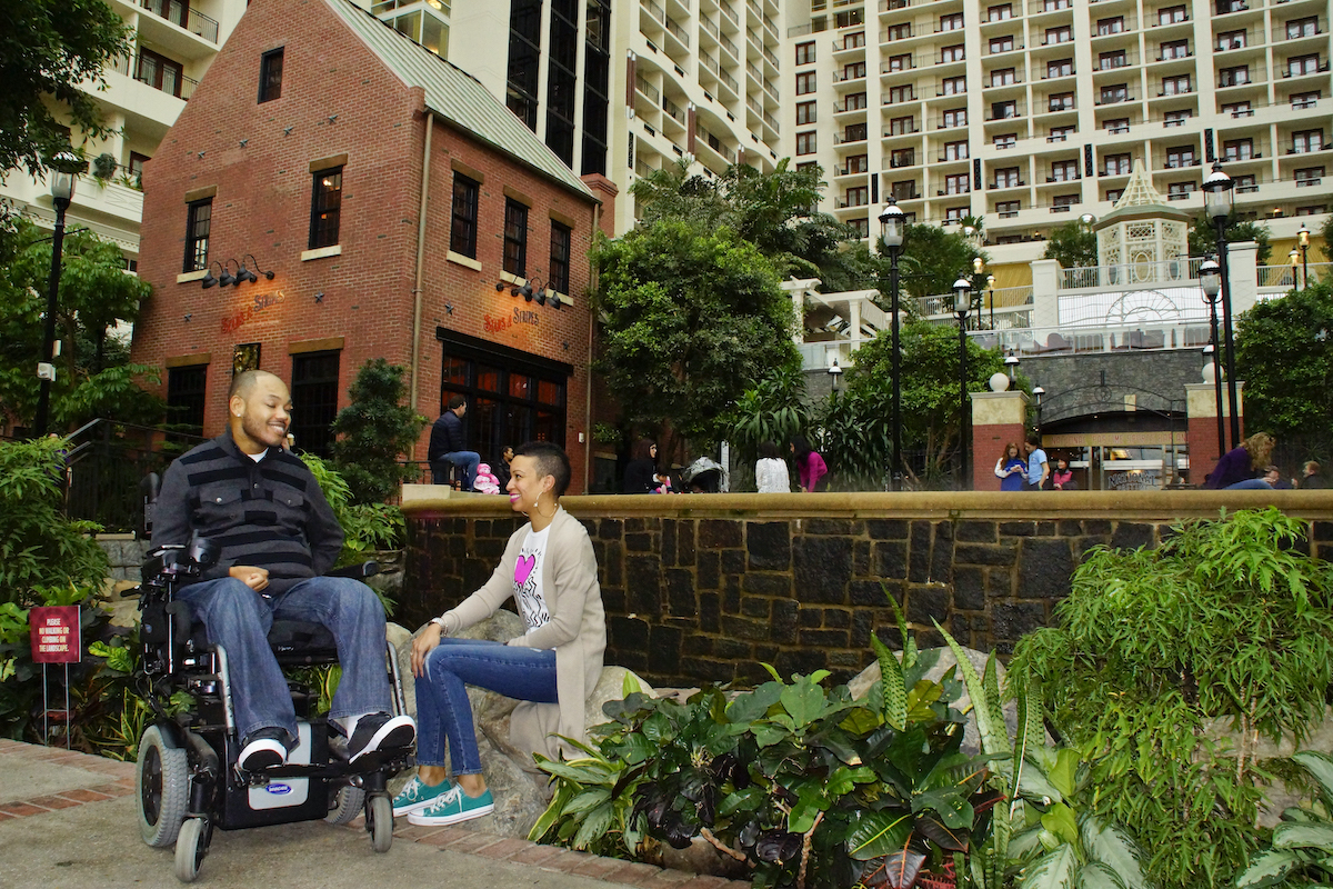 Man smiling and using a wheelchair while looking at a woman sitting and smiling next to him