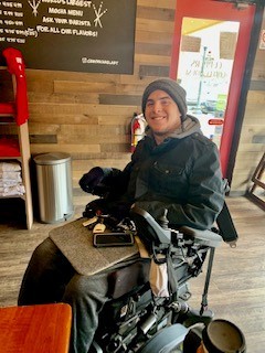 Zack using a wheelchair and smiling