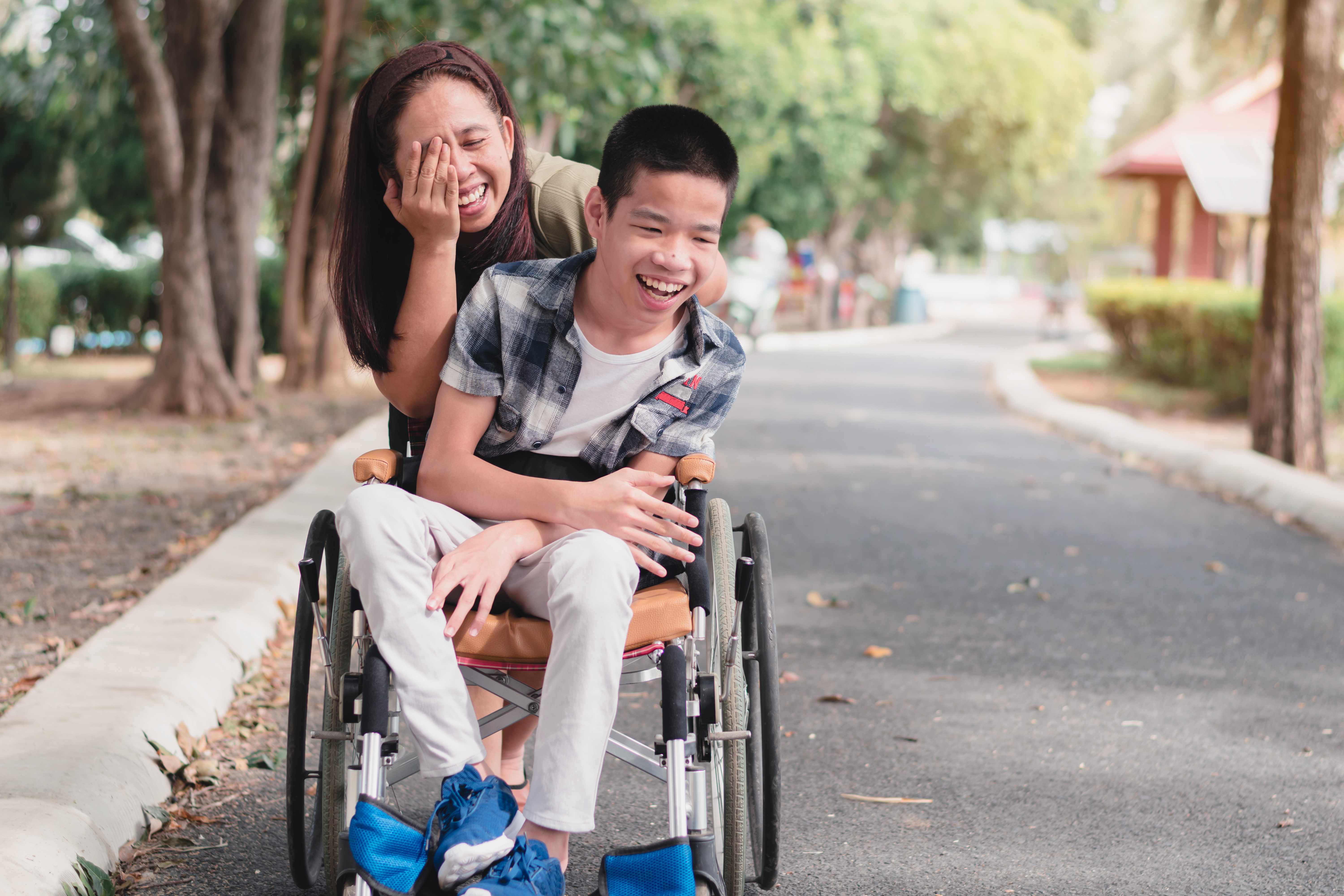 male child laughing in wheelchair with caregiver